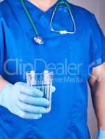 doctor in blue uniform and latex gloves holding a glass of water