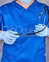 doctor in blue uniform and latex gloves holding a black stethosc