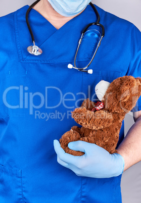 doctor in blue uniform and old latex gloves holding a brown tedd