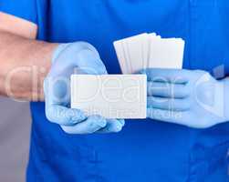 male doctor wearing blue latex gloves is holding a blank white p