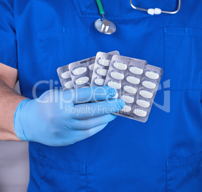 doctor in blue uniform and sterile gloves holding white pills