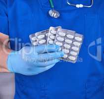 doctor in blue uniform and sterile gloves holding white pills