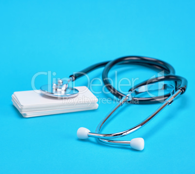 medical stethoscope and empty paper business cards on a blue bac