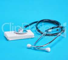 medical stethoscope and empty paper business cards on a blue bac