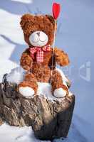brown teddy bear sitting on a stump in the middle of white snow