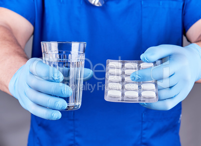 doctor in blue uniform  holds a glass of water and a pack of whi