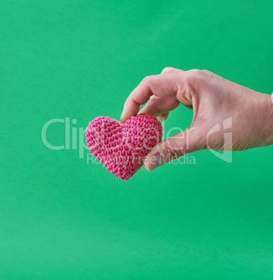 small knitted red heart in a human hand on a green background