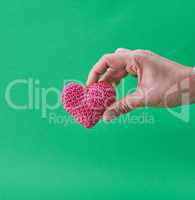 small knitted red heart in a human hand on a green background