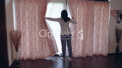 Young woman pulling the curtains in the morning