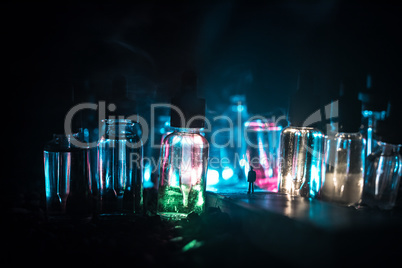 Silhouette of a man standing in the middle of the road on a misty night with giant glass bottles filled with electronic cigarette liquid. Colorful foggy clouds with light on background.