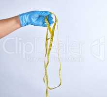 blue sterile gloved hand holding a yellow measuring tape