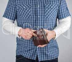 a man in a blue plaid shirt and jeans holds a brown leather purs