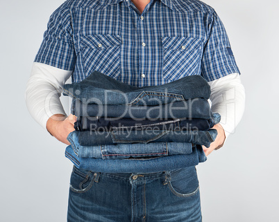 man in jeans and blue plaid shirt holding a pile of jeans