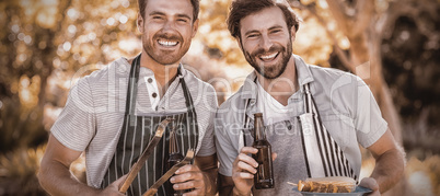 Portrait of two happy men holding barbecue meal and beer bottle