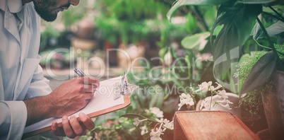 Male scientist writing in clipboard while examining plants