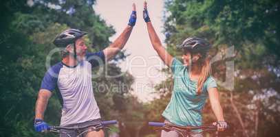 Athletic couple giving high five while riding bicycle on the road