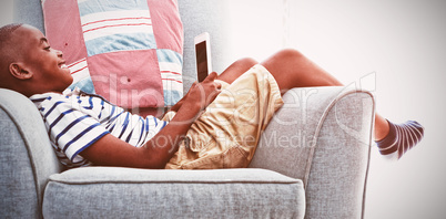 Side view of smiling boy looking at mobile phone while lying on armchair