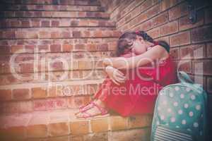 Sad brunette girl seated against a brick wall