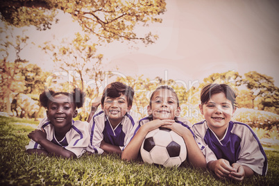 children soccer team smiling at camera while lying on the grass