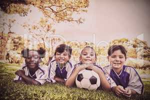 children soccer team smiling at camera while lying on the grass