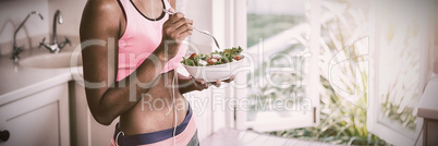 Happy woman having bowl of salad while listening to music