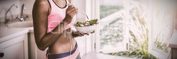 Happy woman having bowl of salad while listening to music