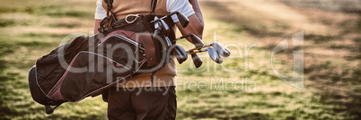 Man carrying golf bag while standing on field