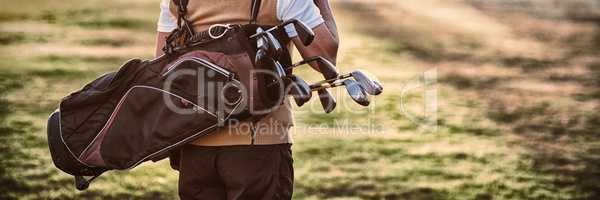 Man carrying golf bag while standing on field