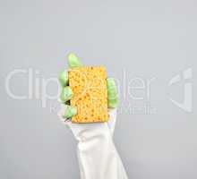 gloved hand holds yellow kitchen sponge