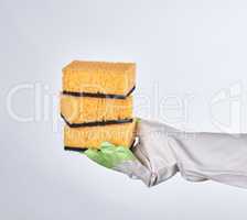 gloved hand holds yellow kitchen sponge