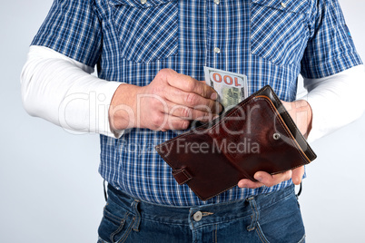 man in a blue plaid shirt and jeans holds a brown leather purse
