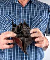 man in blue plaid shirt holds open empty leather wallet