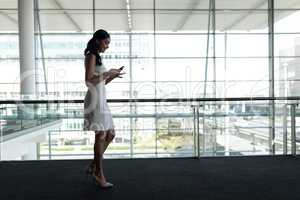 Side view of businesswoman using mobile phone in office and walking on a carpet walkway