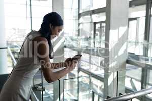 Rear view of businesswoman leaned on the railing and using mobile phone in  office