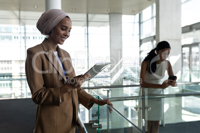 Two businesswoman using digital tablet and mobile phone in first floor of office leaned on the raili