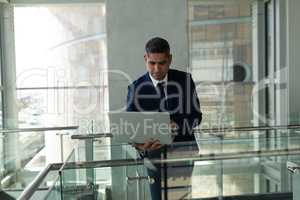 Front view of businessman leaned on the railing and working on his laptop in fisrt floor office