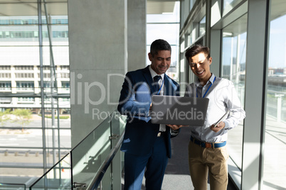 Front view of two businessman standing on the first floor walkway and working on a laptop in office