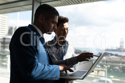 Side view of two businessman standing on the first floor walkway and working on a laptop in office