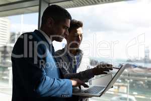 Side view of two businessman standing on the first floor walkway and working on a laptop in office