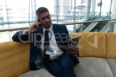 Businessman talking on mobile phone while using digital tablet in office lobby