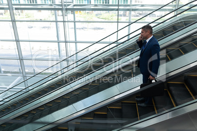 Businessman talking on mobile phone while moving down on escalator