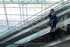 Businessman talking on mobile phone while moving down on escalator