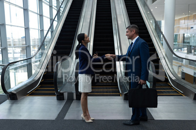 Businessman and businesswoman shaking hands with each other near escalator