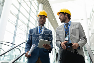 Multi-ethnic male architect discussing over digital tablet at office escalator