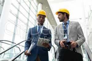Multi-ethnic male architect discussing over digital tablet at office escalator