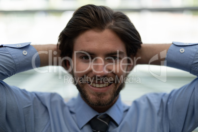 Young Caucasian businessman relaxing with hands behind head in modern office