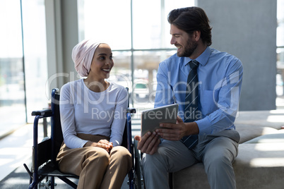 Happy disabled mixed-race female executive with Caucasian businessman discussing over digital tablet