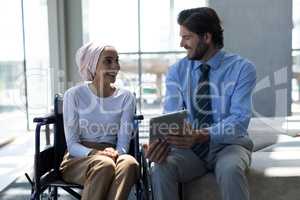 Happy disabled mixed-race female executive with Caucasian businessman discussing over digital tablet