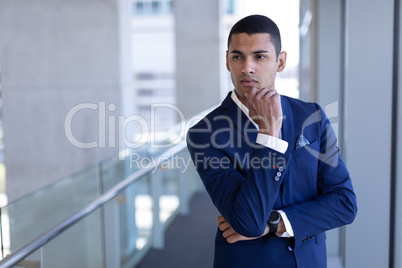 Front view of young businessman with hand on chin looking away in office