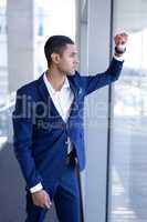 Side view of young mixed-race businessman looking through window standing in modern office